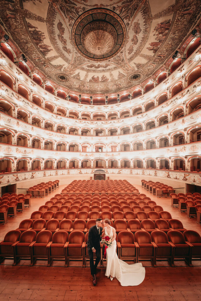 Coppia di sposi si bacia nell'elegante teatro con poltrone rosse.