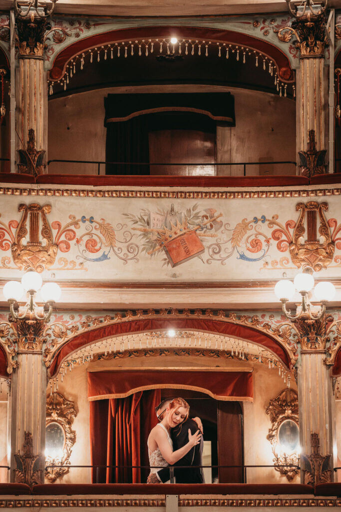 Coppia abbracciata in un teatro storico con decorazioni dorate.