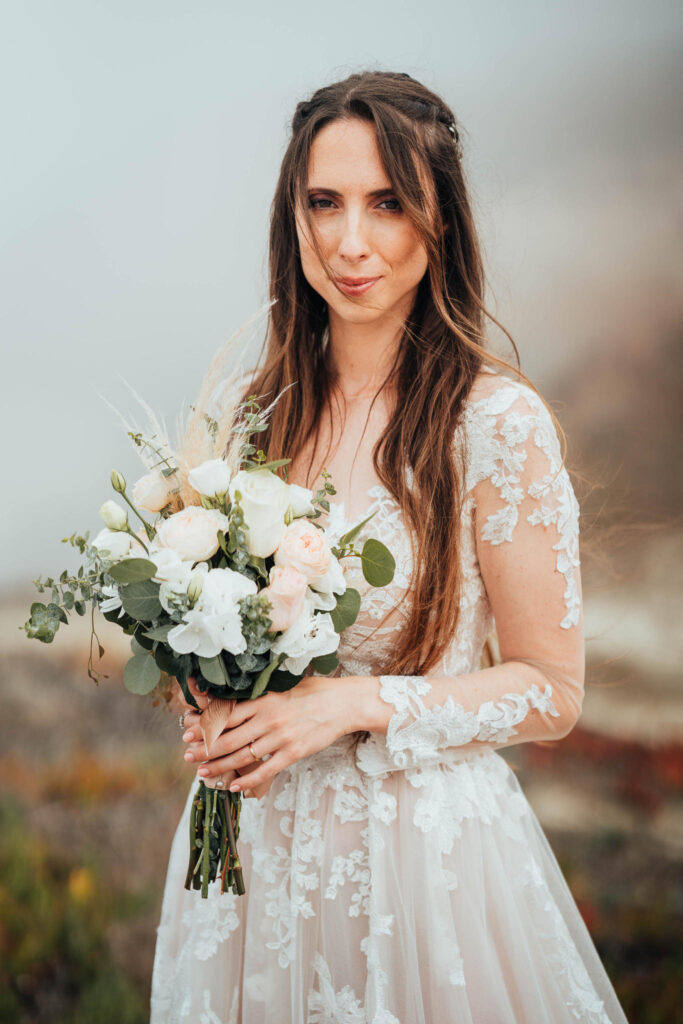 Sposa con bouquet di rose e fiori bianchi in abito di pizzo.